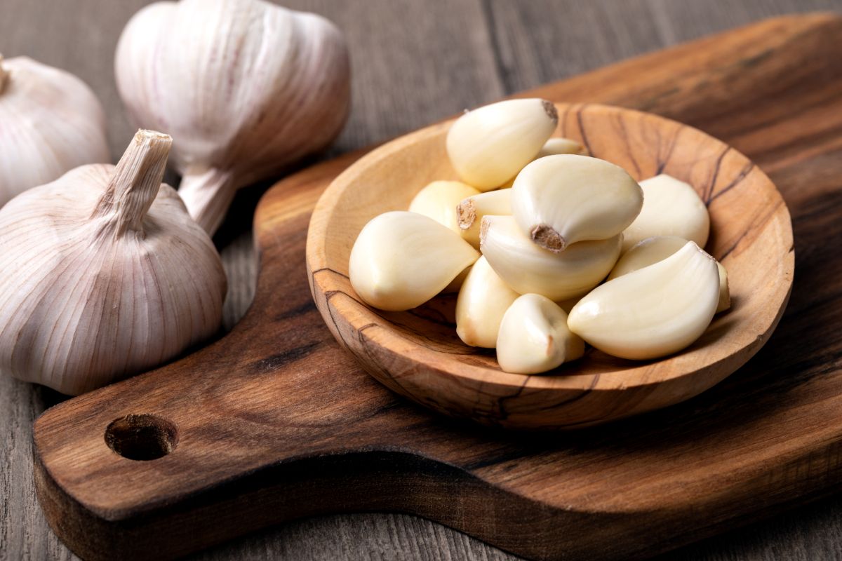 Triimed galirc in a wooden bowl on a board next to garlic heads.