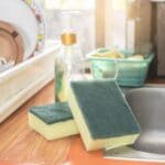 Two kitchen sponges on a kitchen table next to a washbasin.