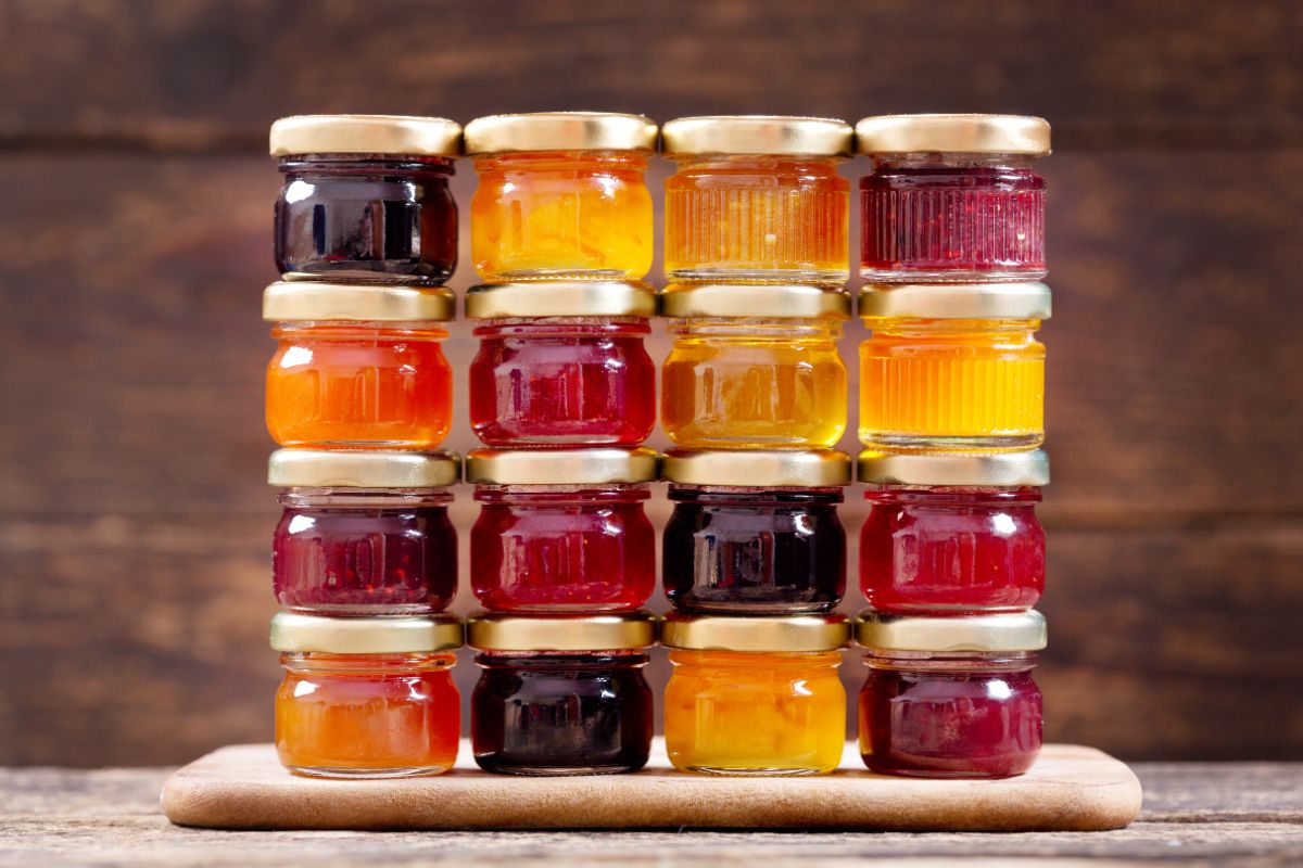 Piles of different vaieties of jams in jars on  a wooden board.