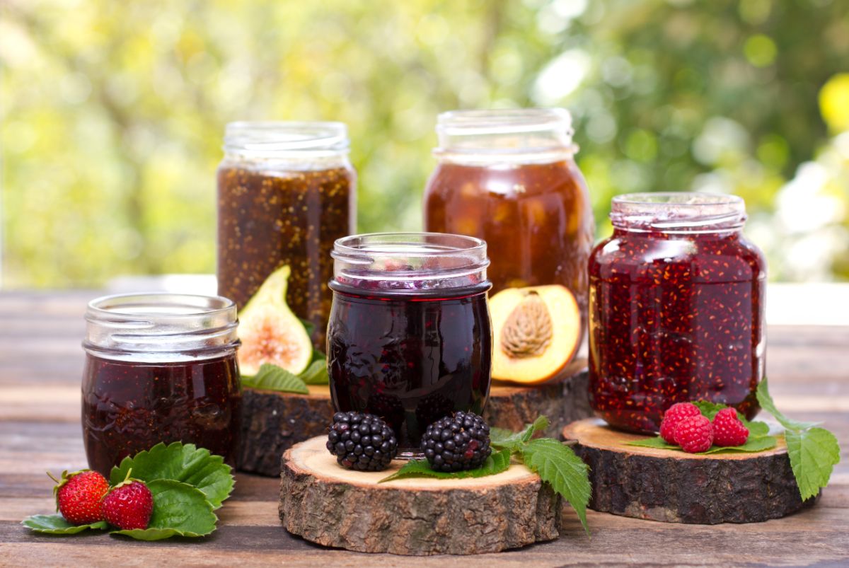 Different varieties of jam in glass jars on a wooden table with fruits around.