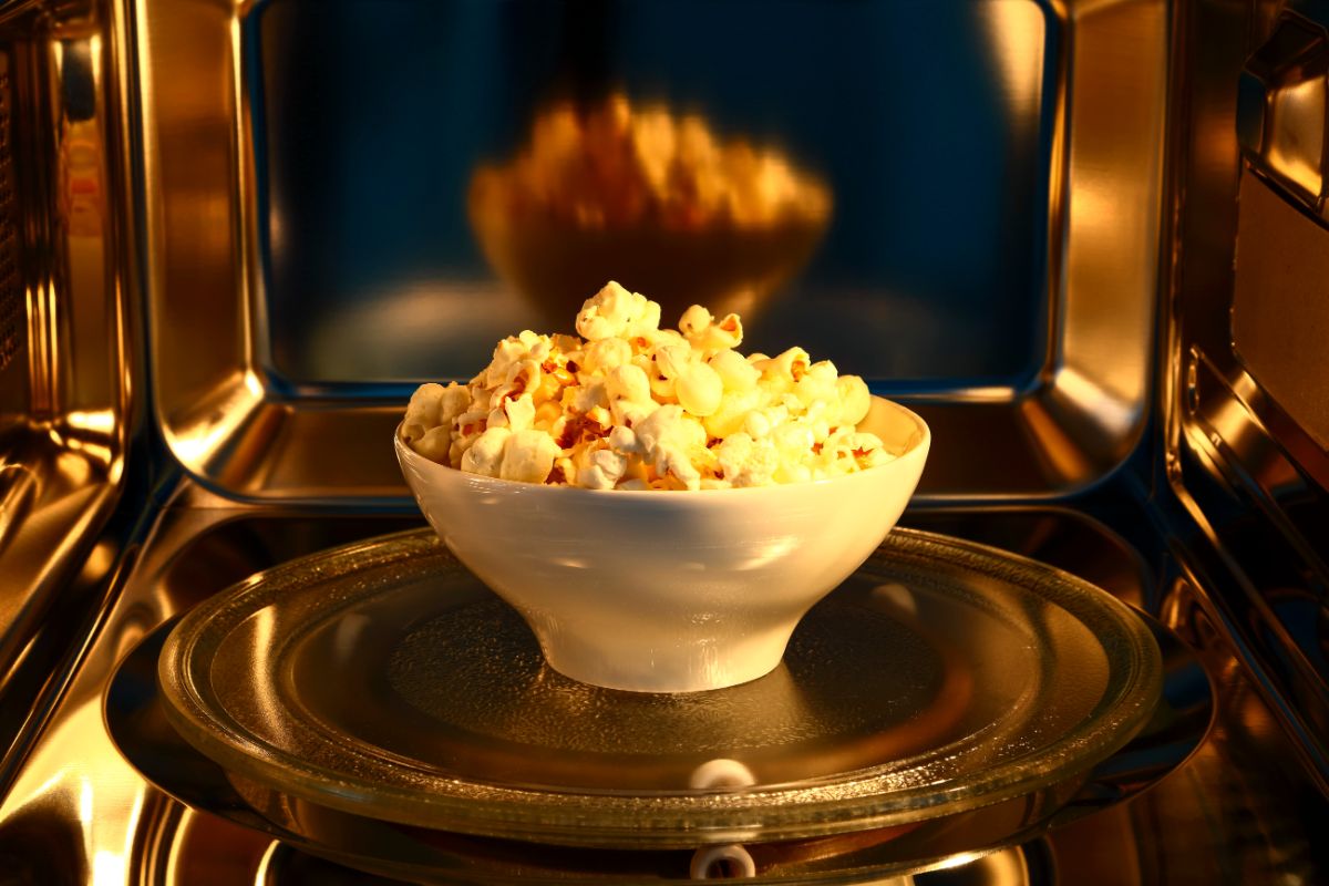 White bowl of popcorn in a microwave.