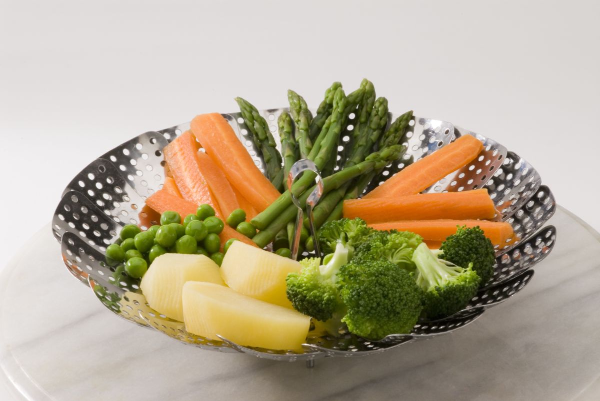 Vegetable steamer with varieties of vegetable on a table.