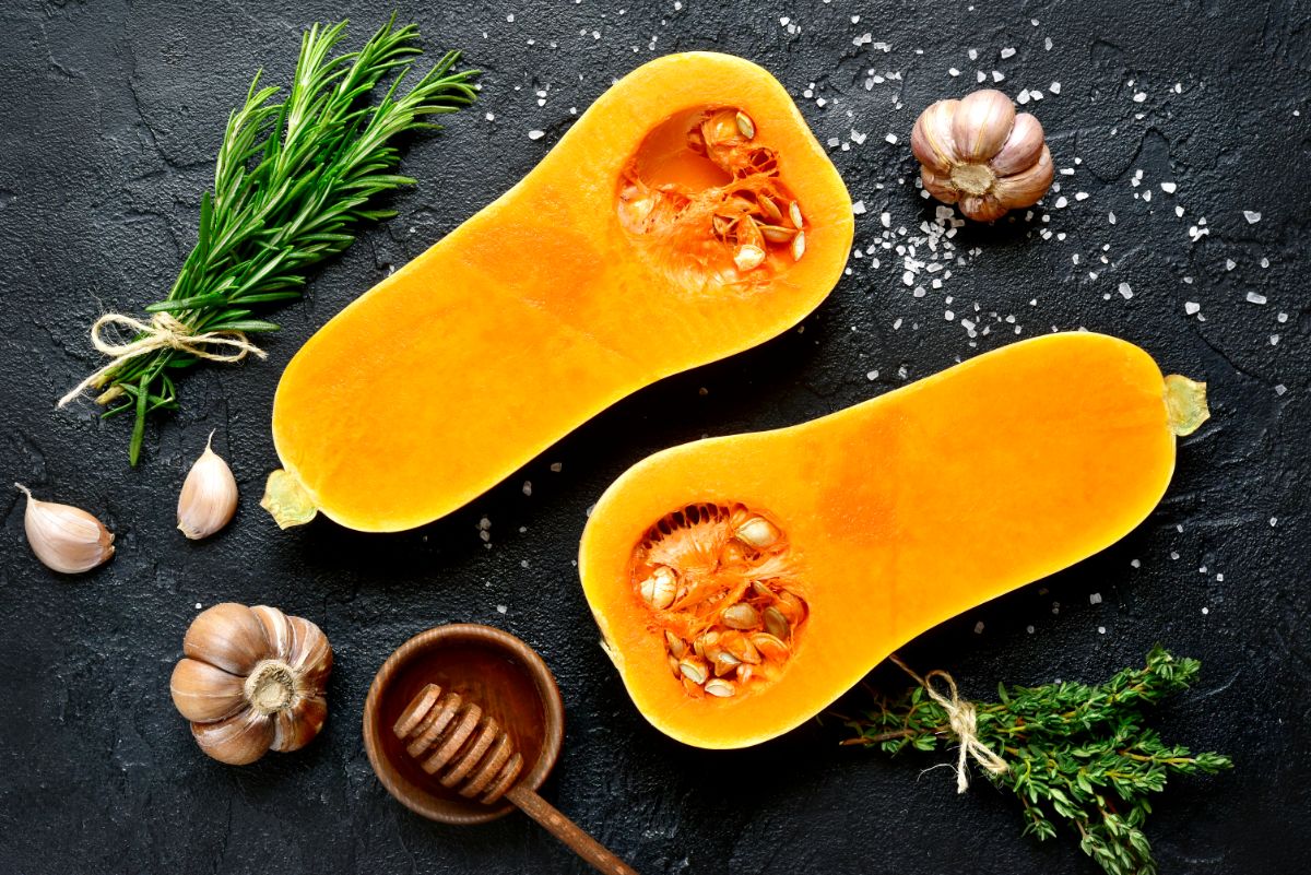 Two half os butternut squash with bowl of honey and heads of garlic on a table.