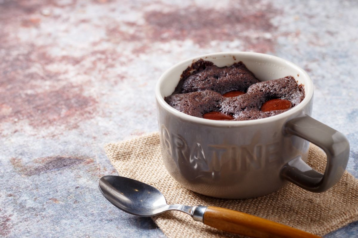 Ceramic mug full of a cake wuth a spoon on a table.