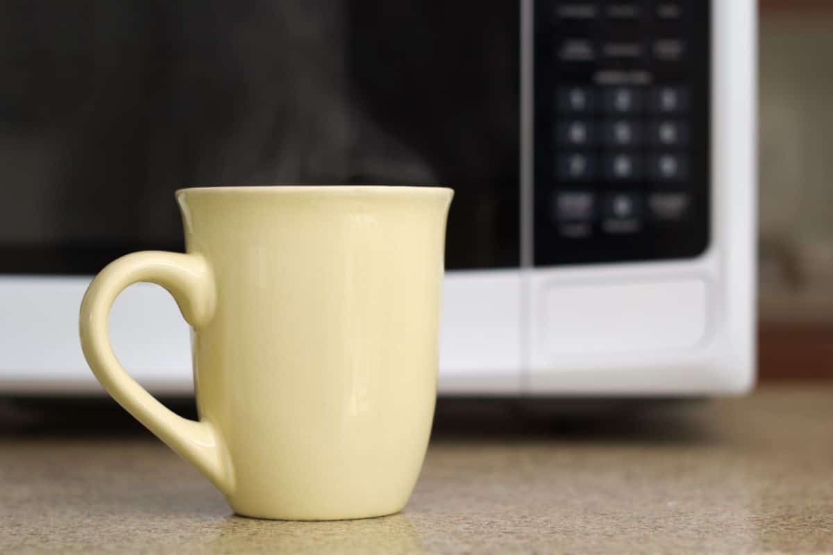 Yellow ceramic mug infront of a microwave.