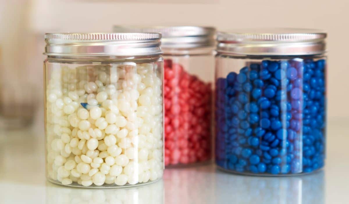 Three glass jars with colorful wax beads on a table.