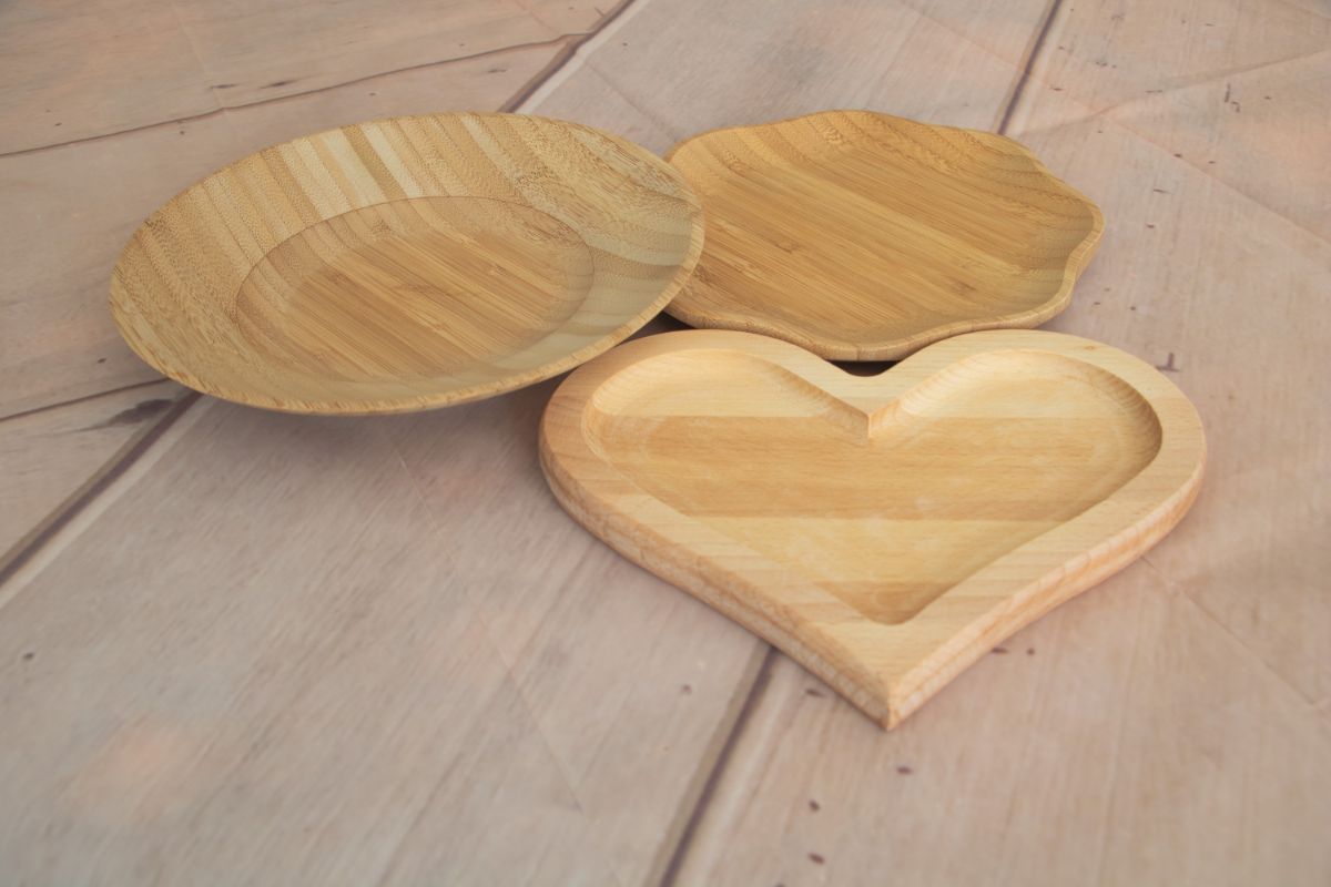Two bamboo plates and one heart-shaped wooden plate on a wooden table.
