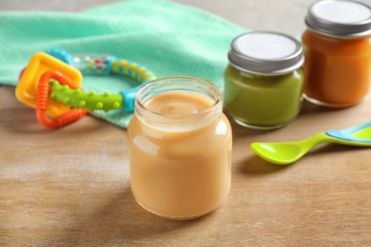 Three glass jars of baby food with a spoon and a soother on a table.