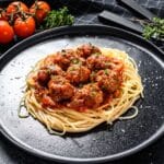 Spaghetti with meatballs on a black plate.