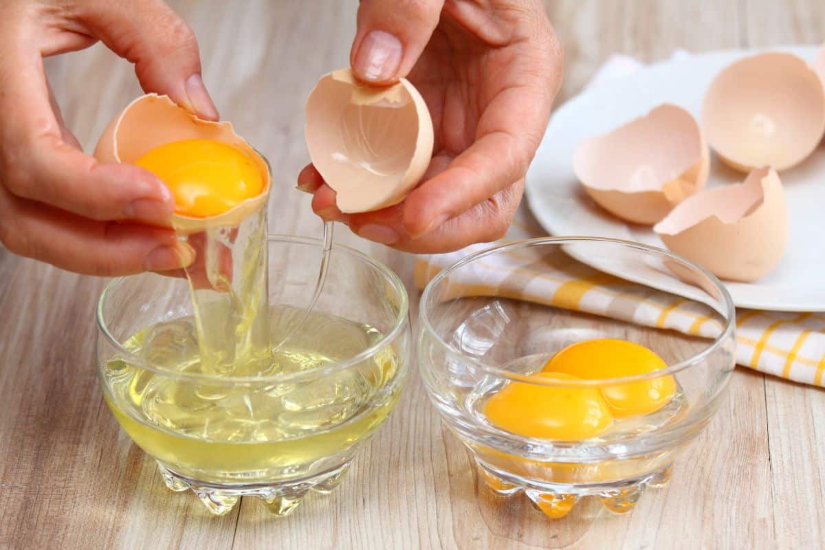 A chef breaking eggs and separating egg whites and folks.