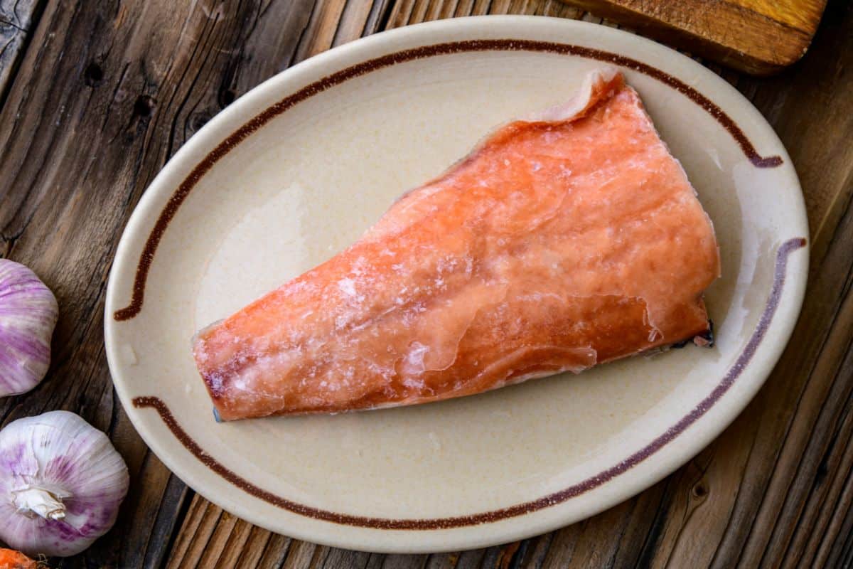 A frozen salmon fillet on a plate on a wooden table.