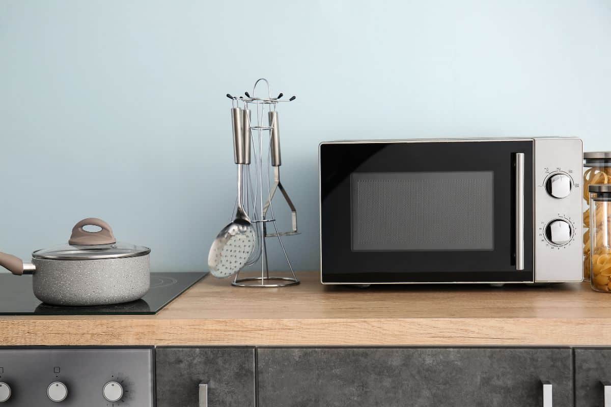 A new microwave on a kitchen counter with kitchen water and a pot.