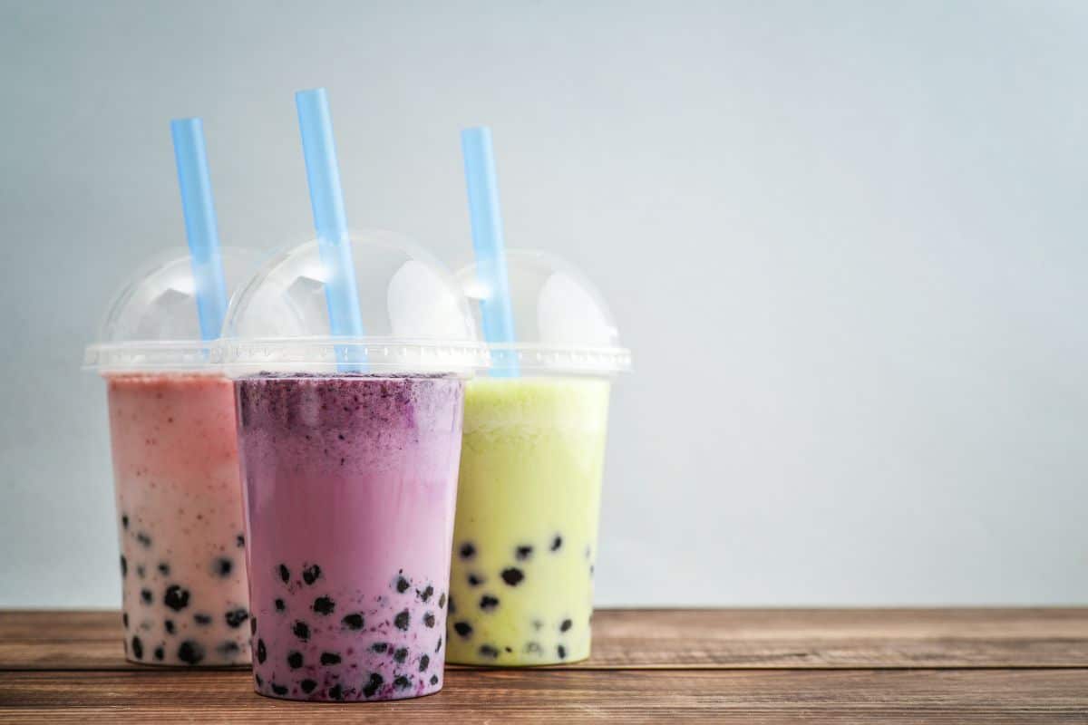 Three plastic cups full of tea with straws on a wooden table.