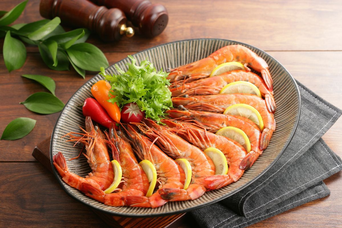 A plate full of shrimp, slices of lemons, and vegetables on a wooden table.