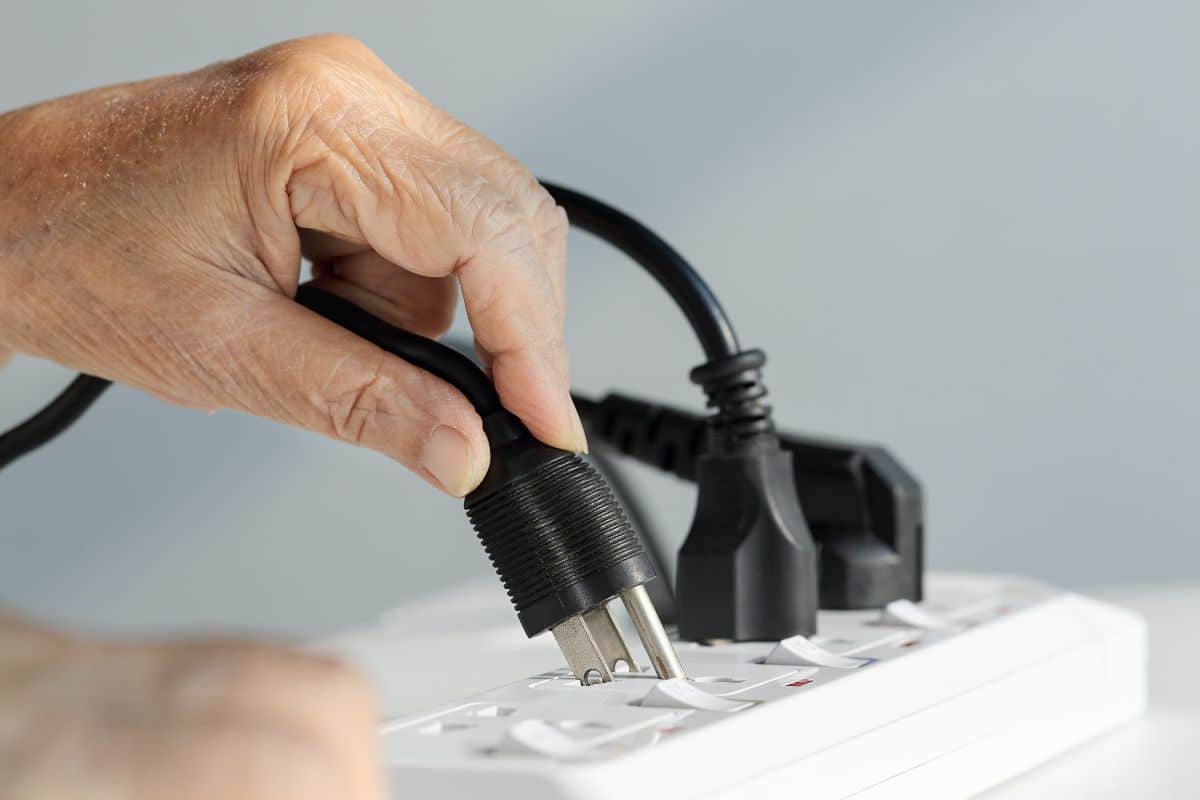 A hand plugging power plug into a power outlet.