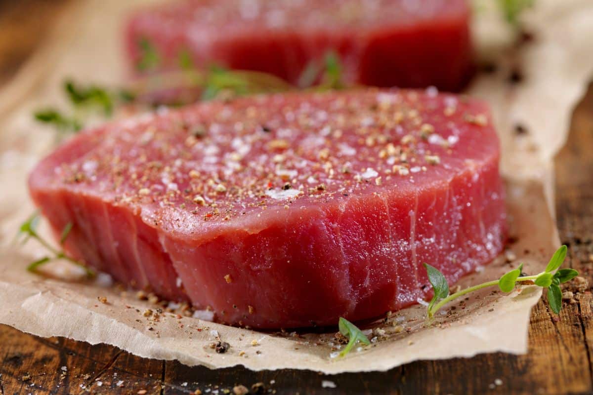 A close-up of a seasoned raw steak on parchment paper on a wooden table.