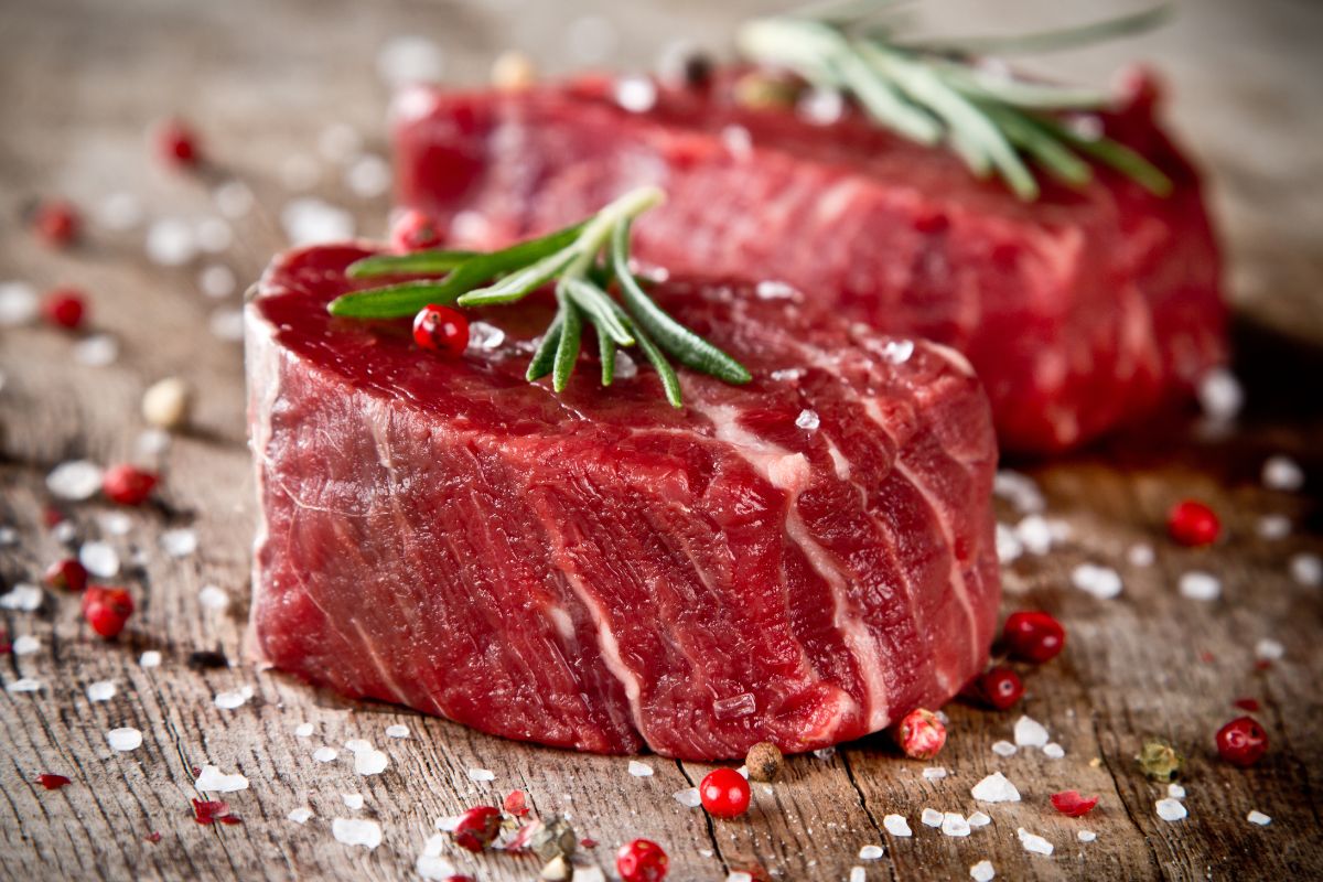 A close-up of a seasoned raw steak on a wooden table.