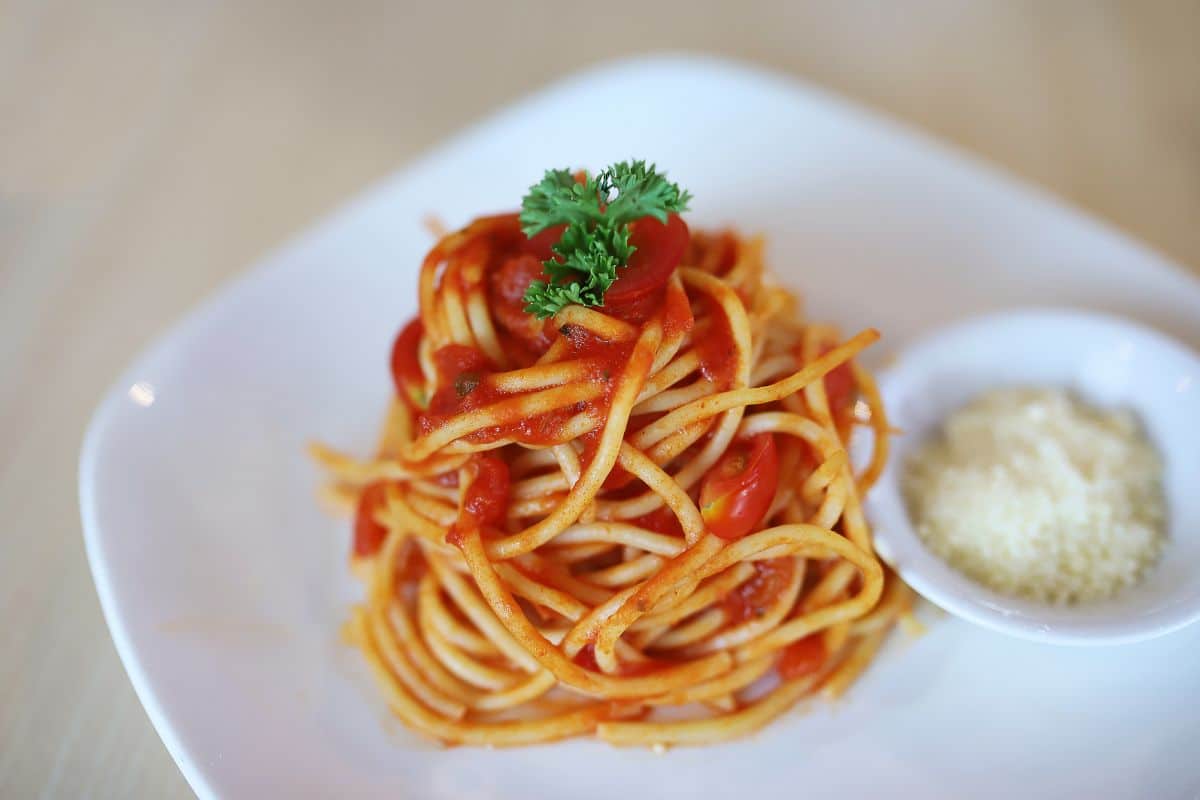 Spaghetti with sauce and a herb on a white plate with a small bowl of cheese.