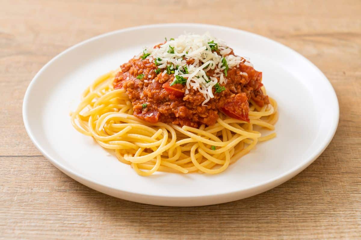 A white plate full of tasty spaghetti with cheese and sauce on a wooden table.