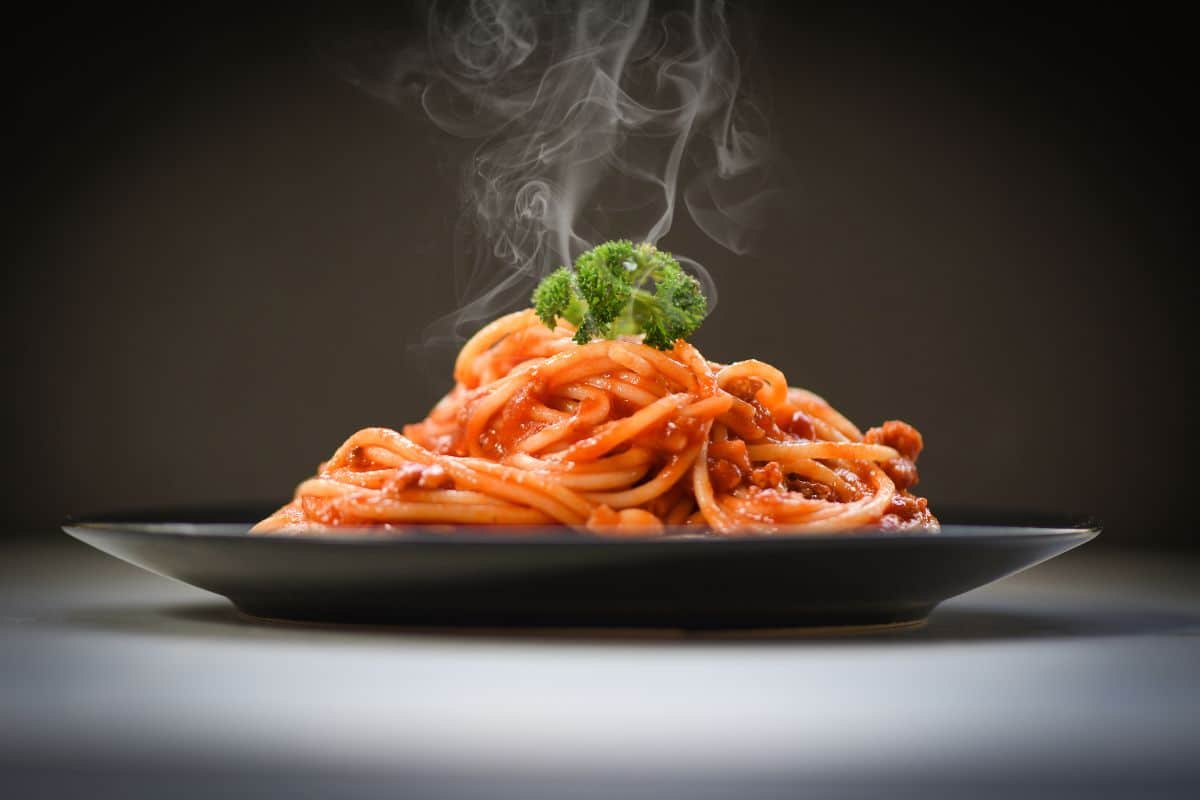Steaming spaghetti with sauce and broccoli on a black plate.