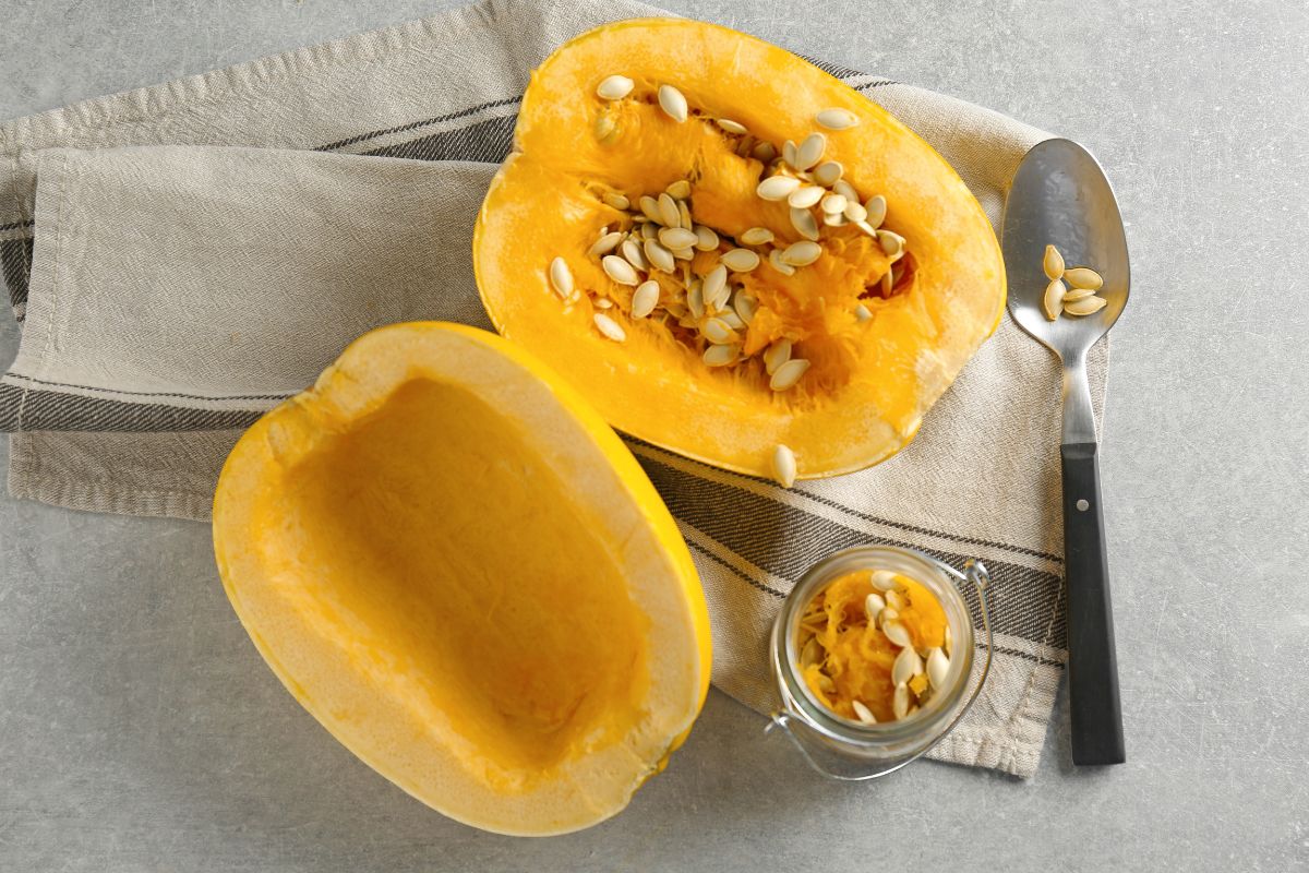 Two halves os spaghetti squash on a table with a spoon and a small glass jar.