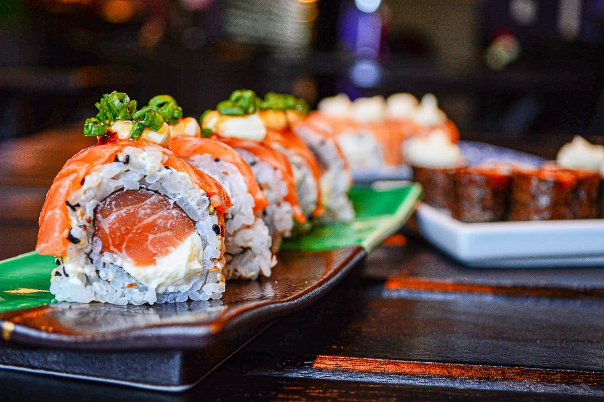 A bunch of sushi rolls on a black tray.