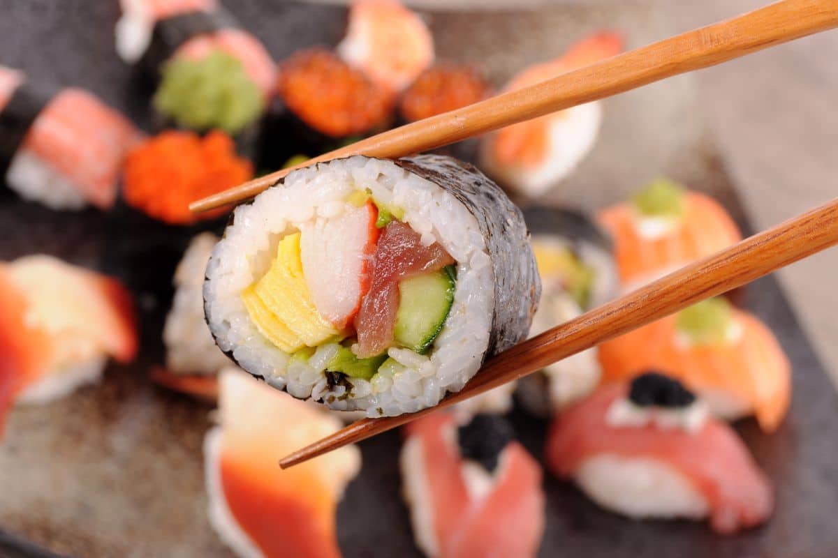 A close-up of a sushi roll held by chopsticks.