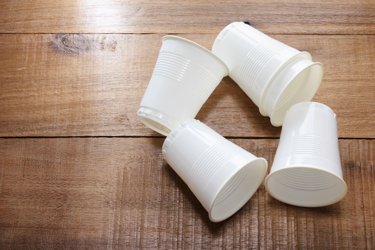 Five white plastic cups on a wooden table.