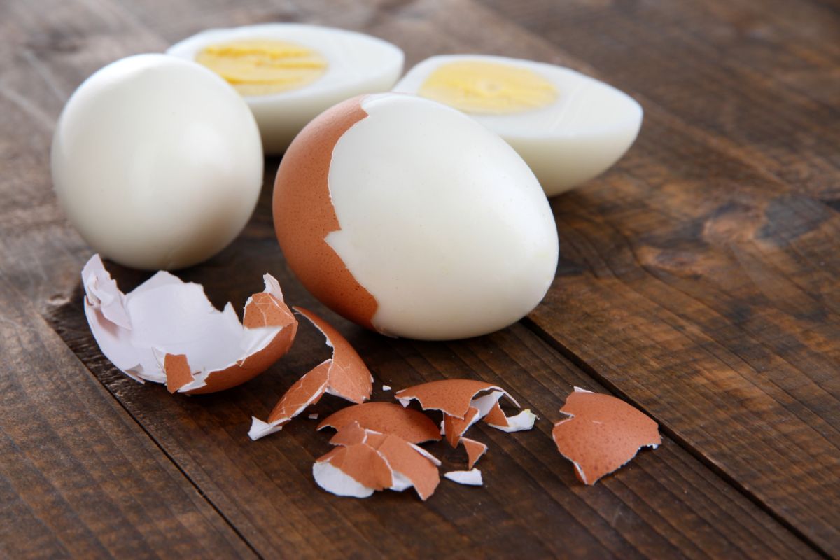 Hard-boiled eggs partially peeled on a wooden table.