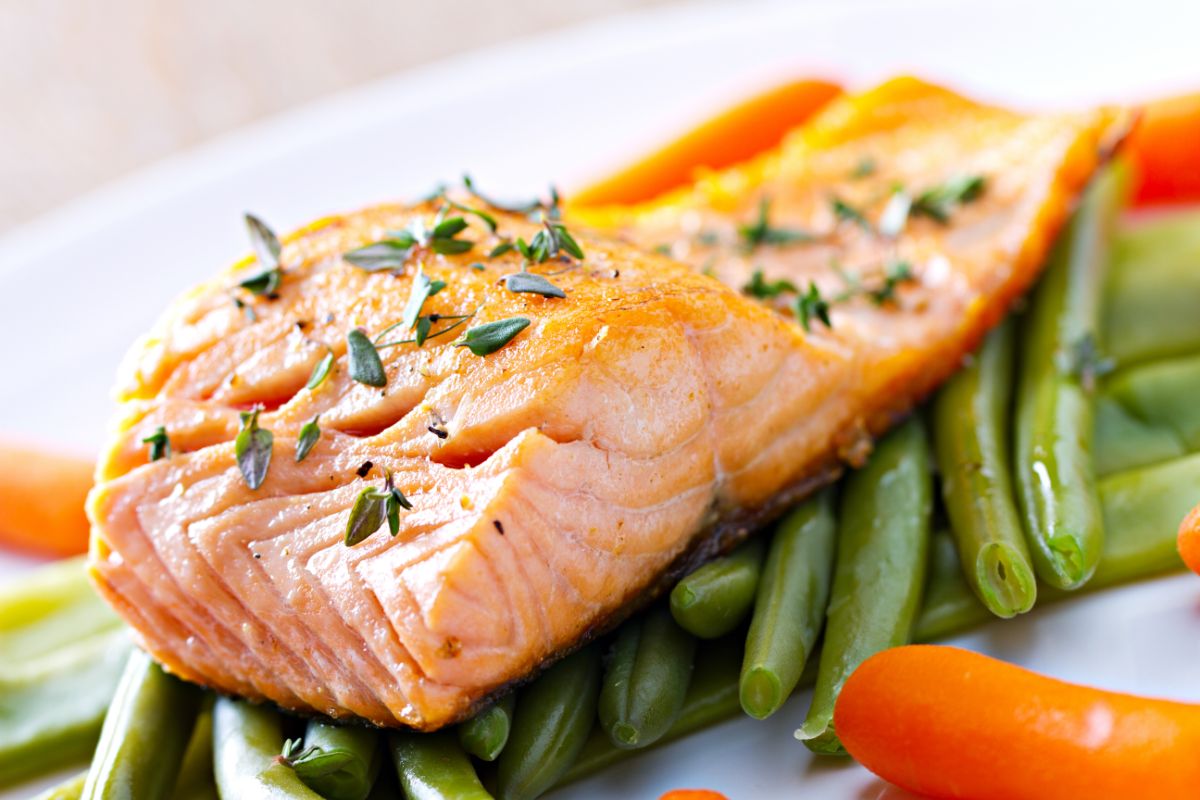 A piece of salmon with greens on a white plate.