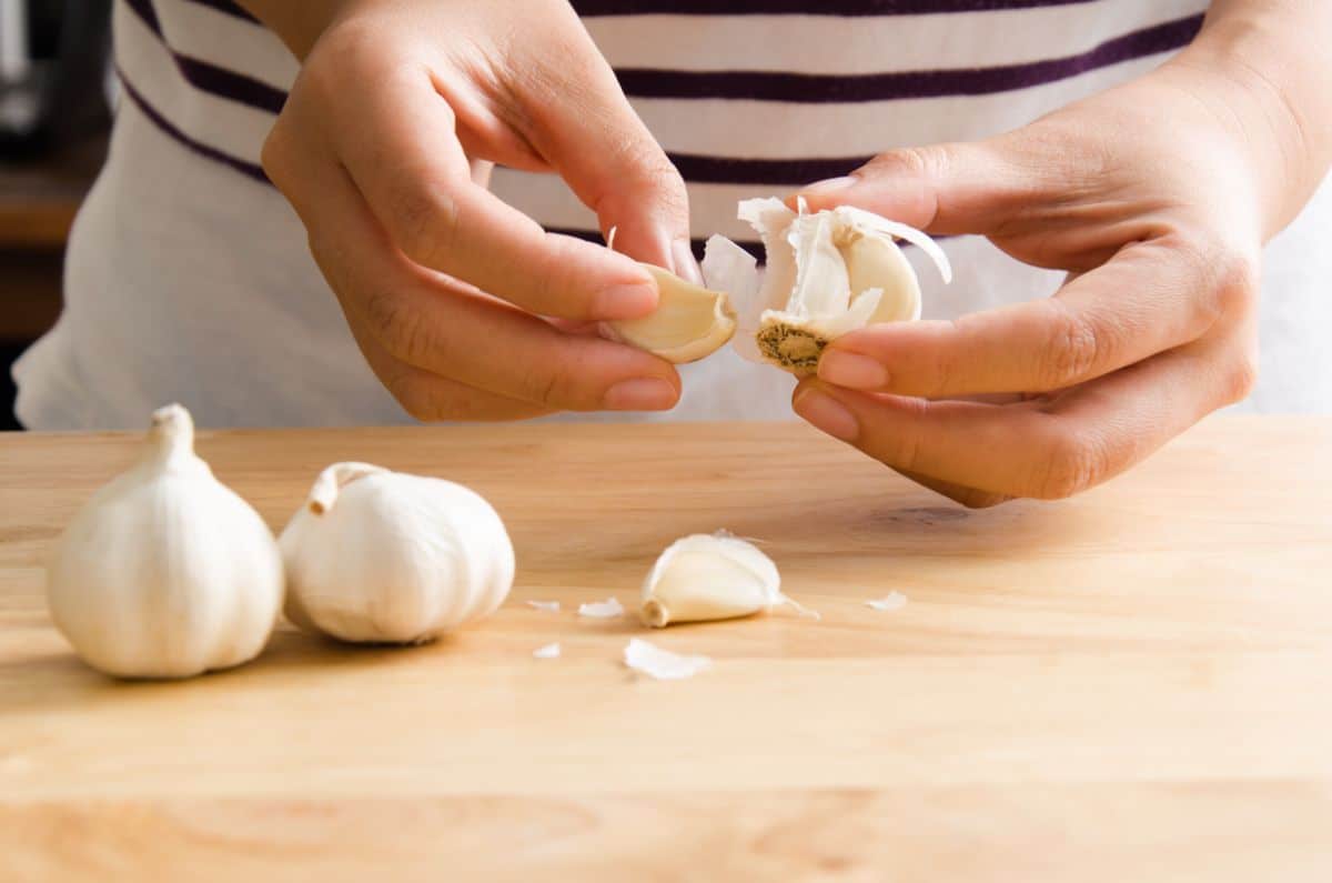 Hands peeling garlic on a wooden board.