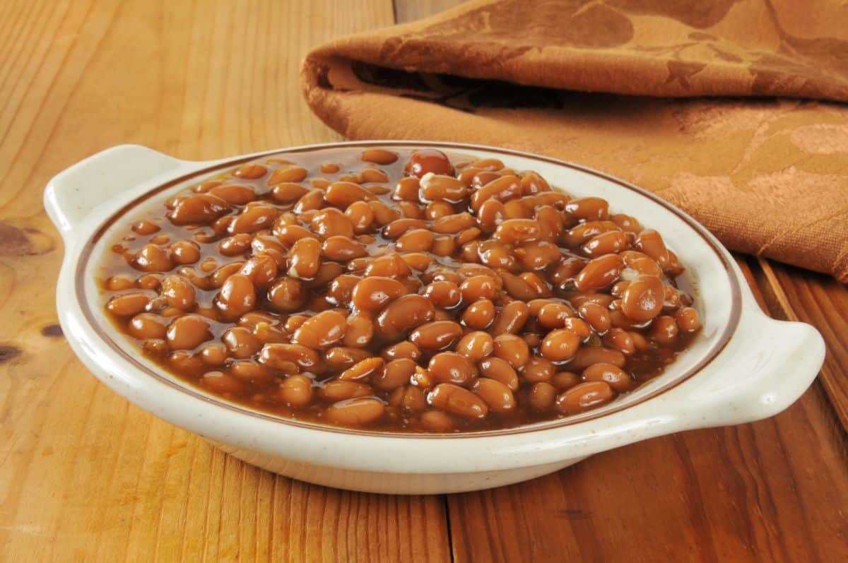 A plate full of cooked beans on a wooden table.