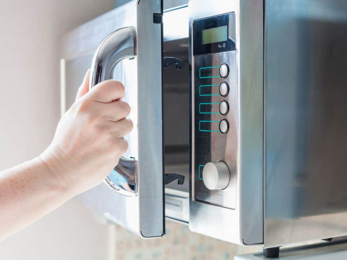 A hand opening a microwave by a microwave latch.