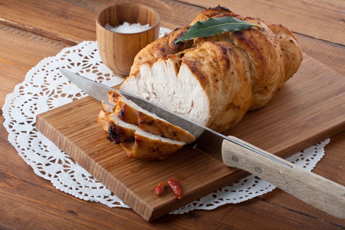 Baked turkey partially sliced on a wooden cutting board with a knife.