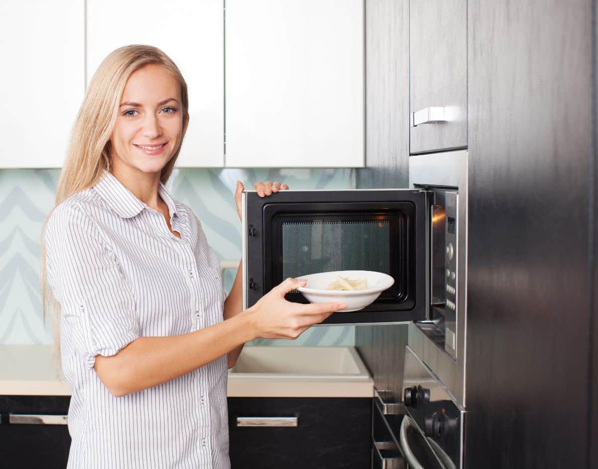 A young woman putting a dish into a microwave.