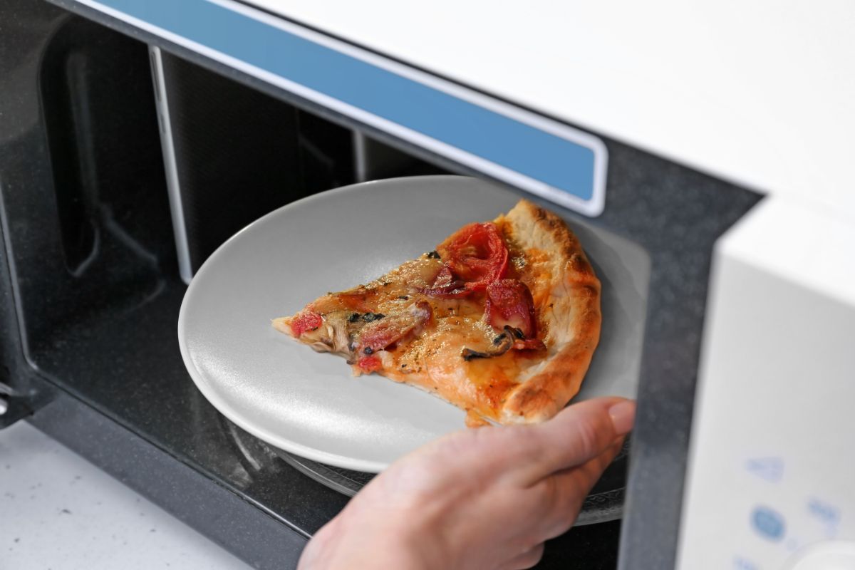 A hand putting a pizza slice on a white plate in a microwave.