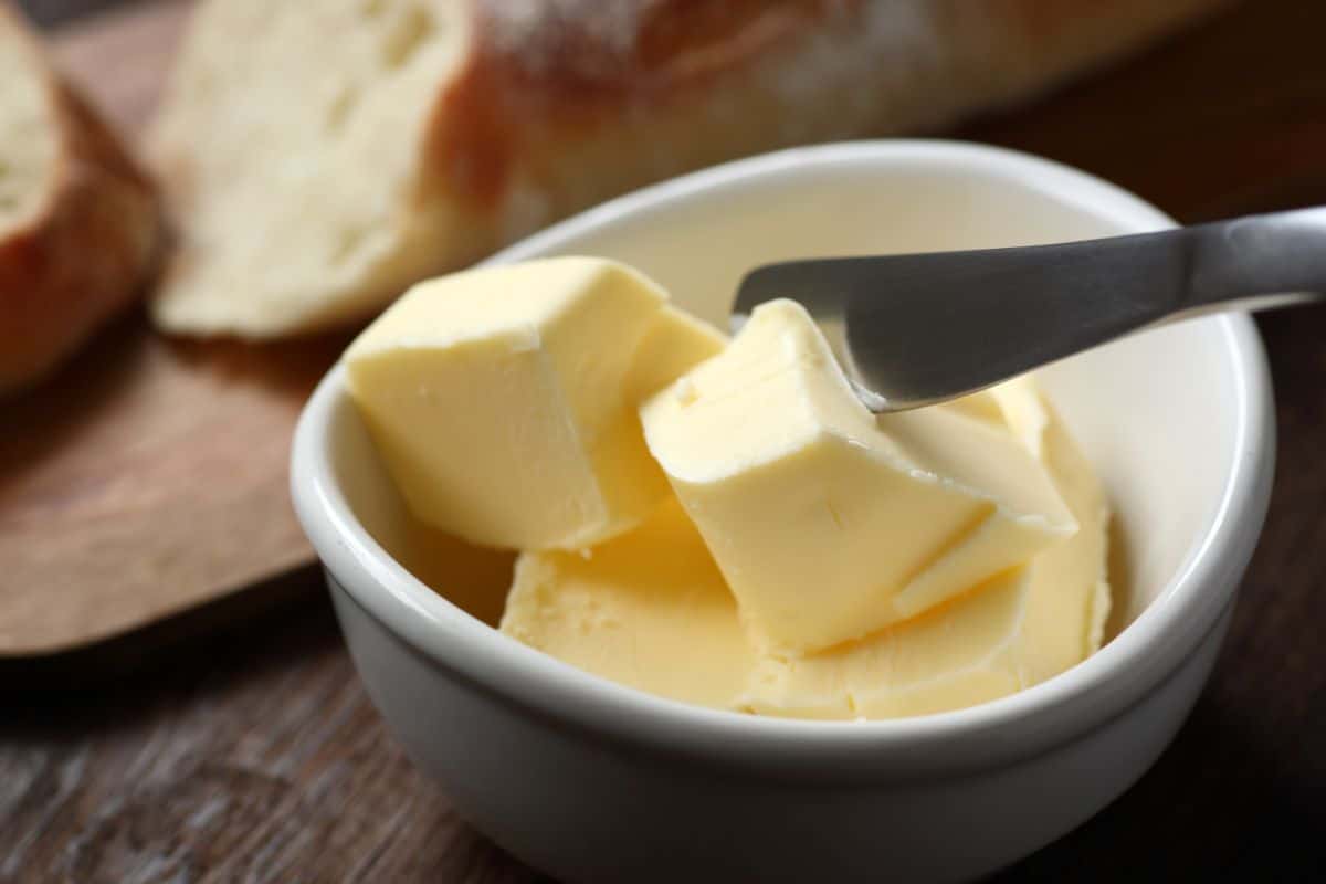 A bowl of butter with a knife on a wooden table.
