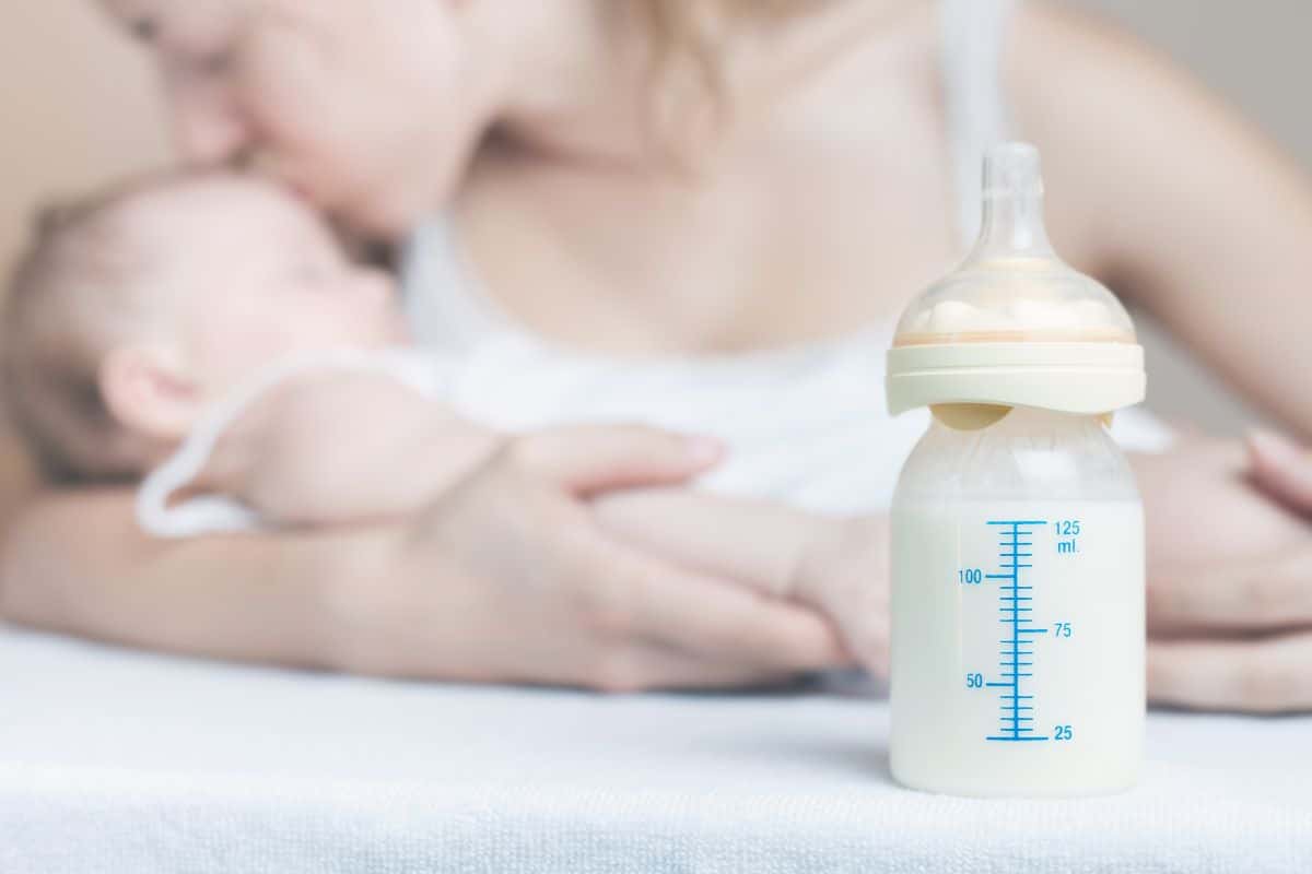 A bottle of breast milk with a baby and mother in the background.