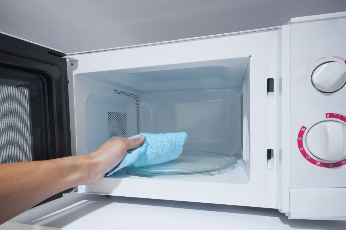 A hand with a blue wipe cleaning a microwave.