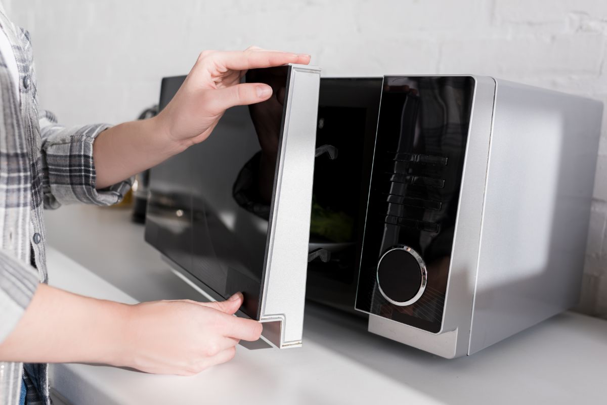 A woman closing a microwave doors.