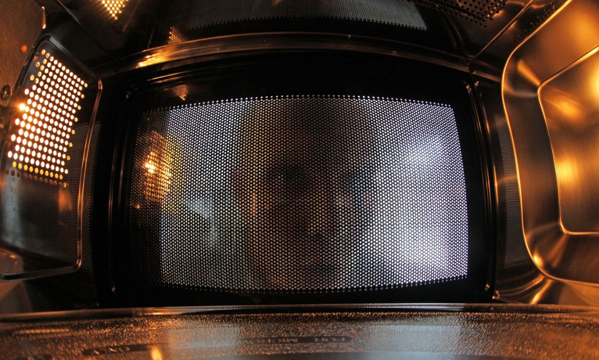 A man looking though a microwave door inside a microwave.