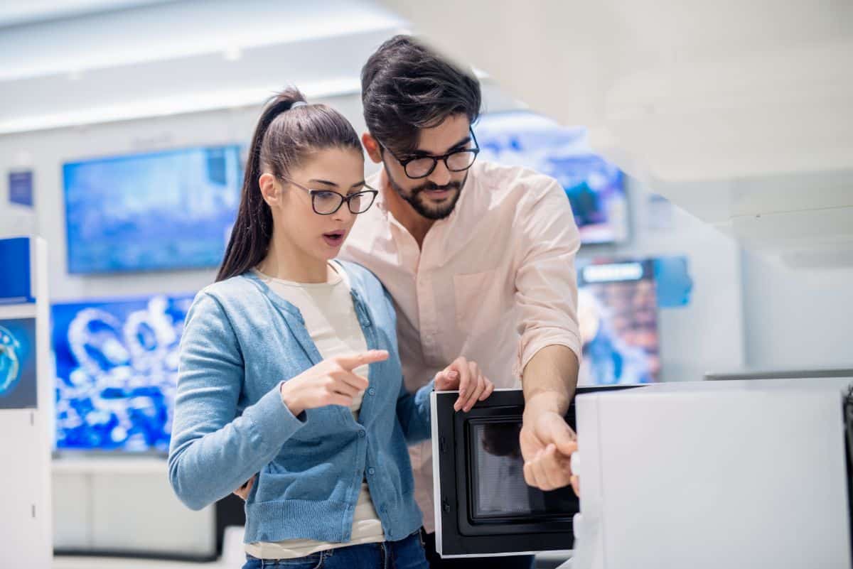 A young couple looking at a microwave in a store.