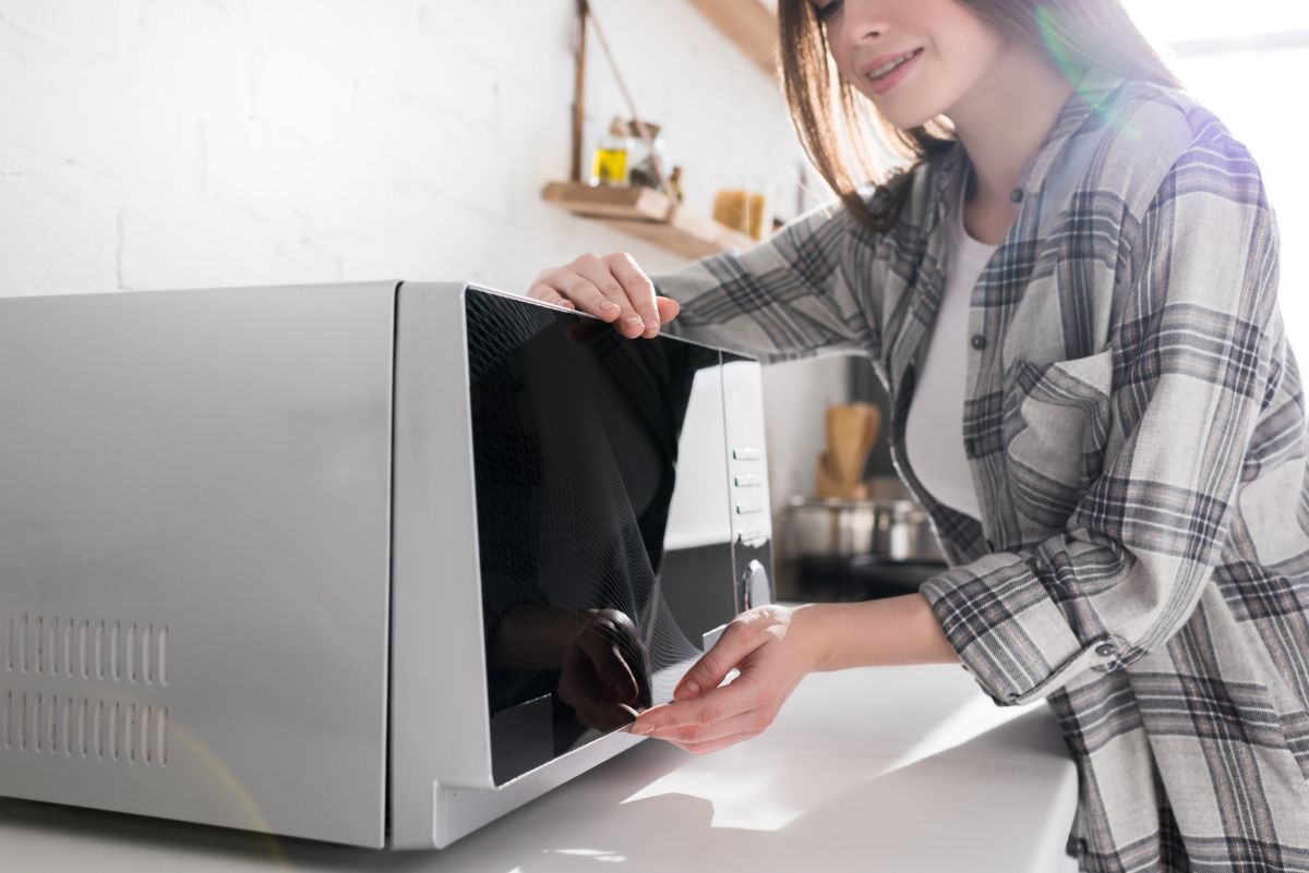 A young woman using a microwave in a kitchen.