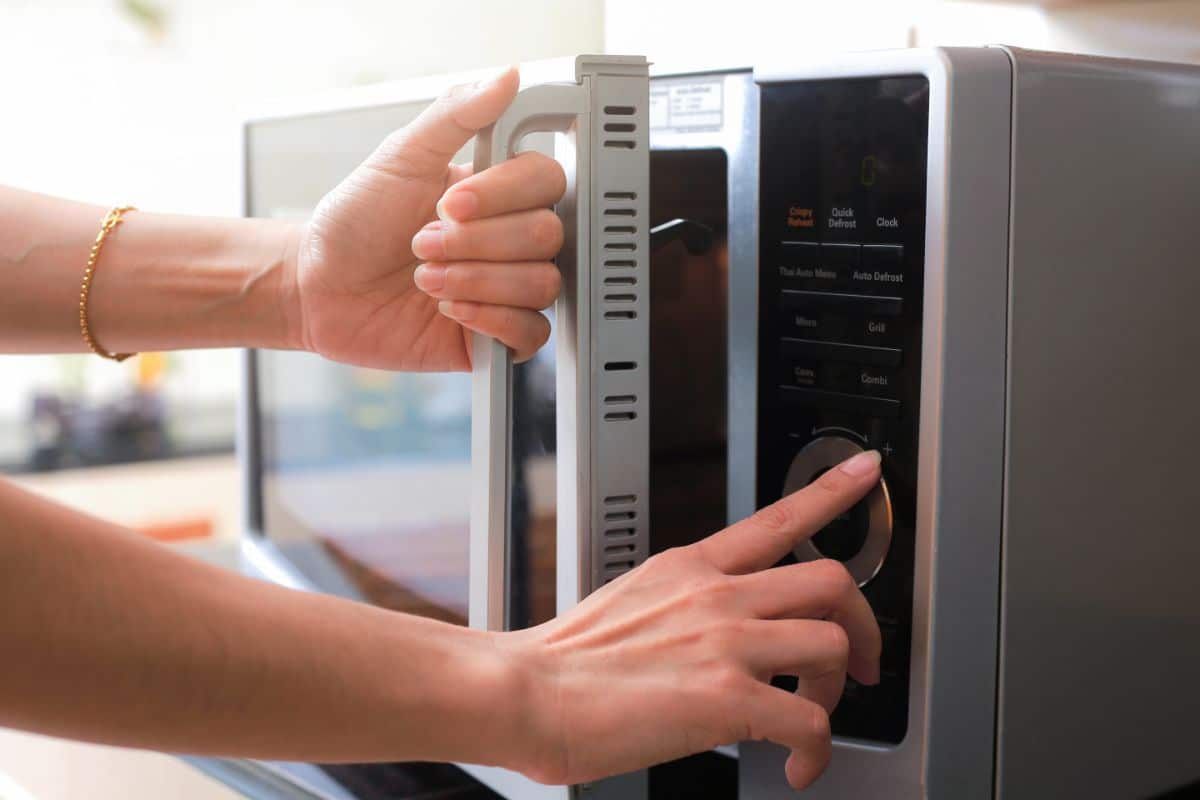 Hands set microwave and holding a microwave handle.