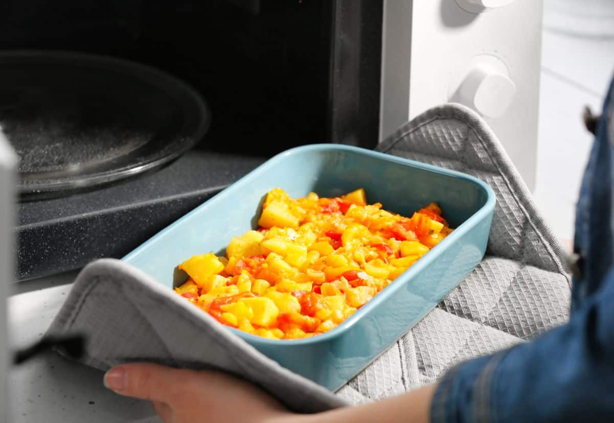 A blue casserole on a mat in front of a microwave.