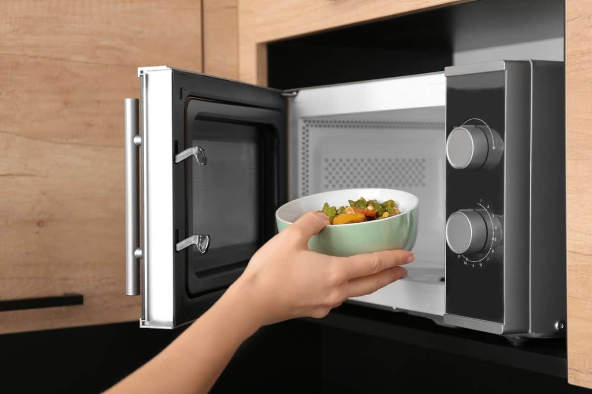 A hand putting a bowl of food in a microwave.