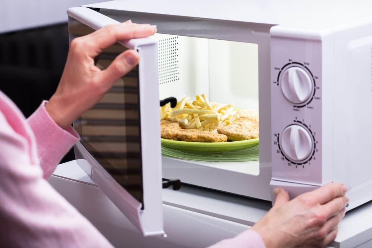 A man setting up a microwave to heat up a meal on a plate.