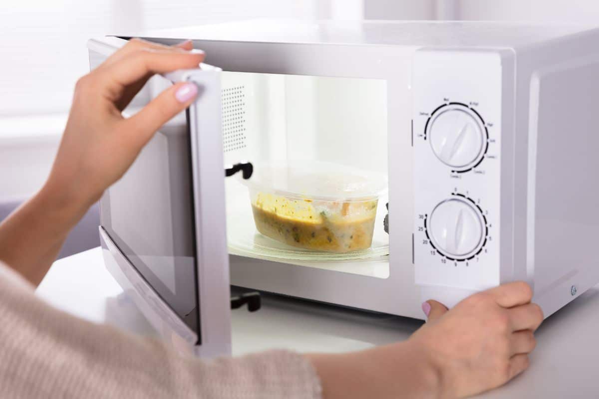 A woman setting up a microwave to heat a meal in a plastic container.