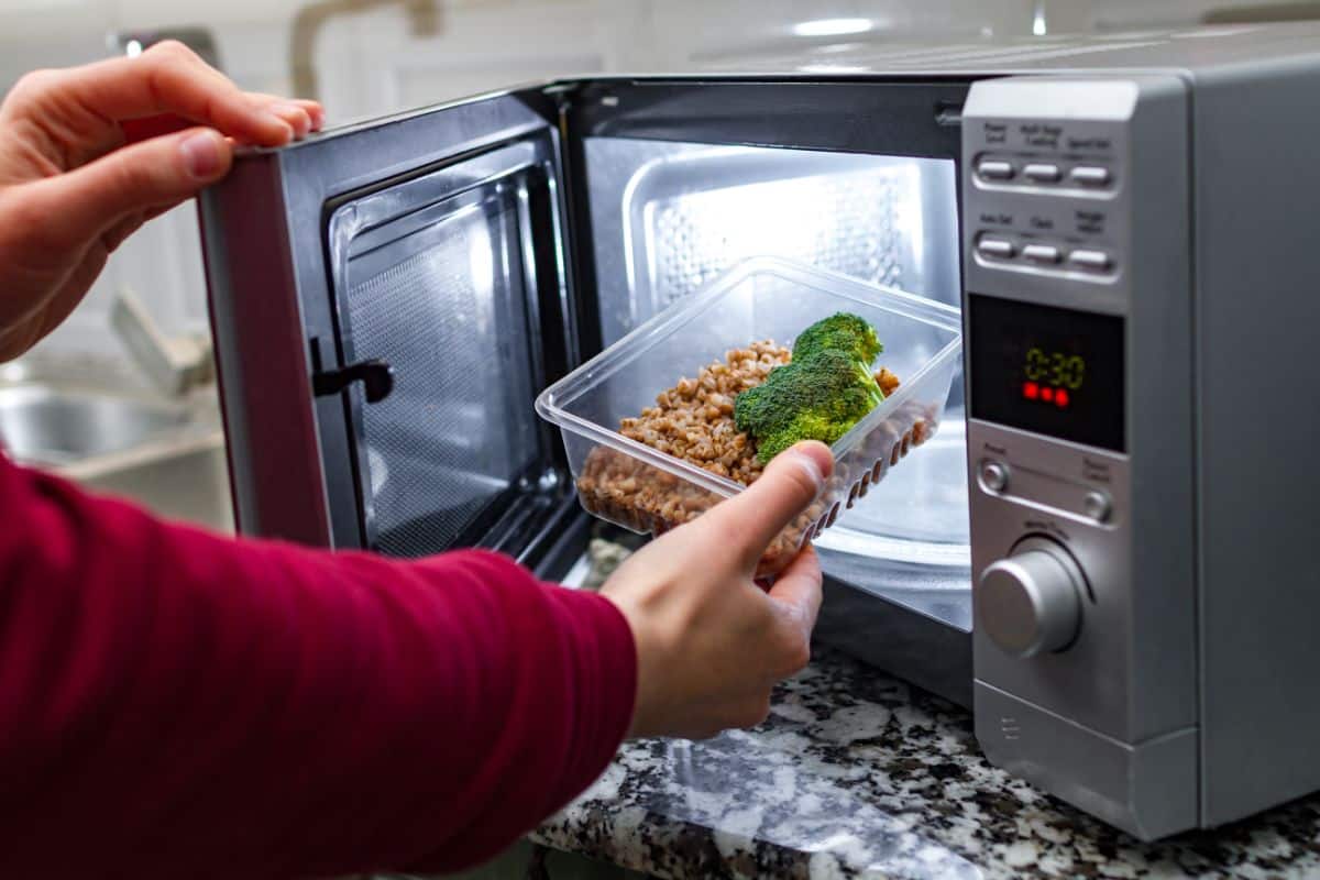 A man putting a meal in a plastic container in a microwave.