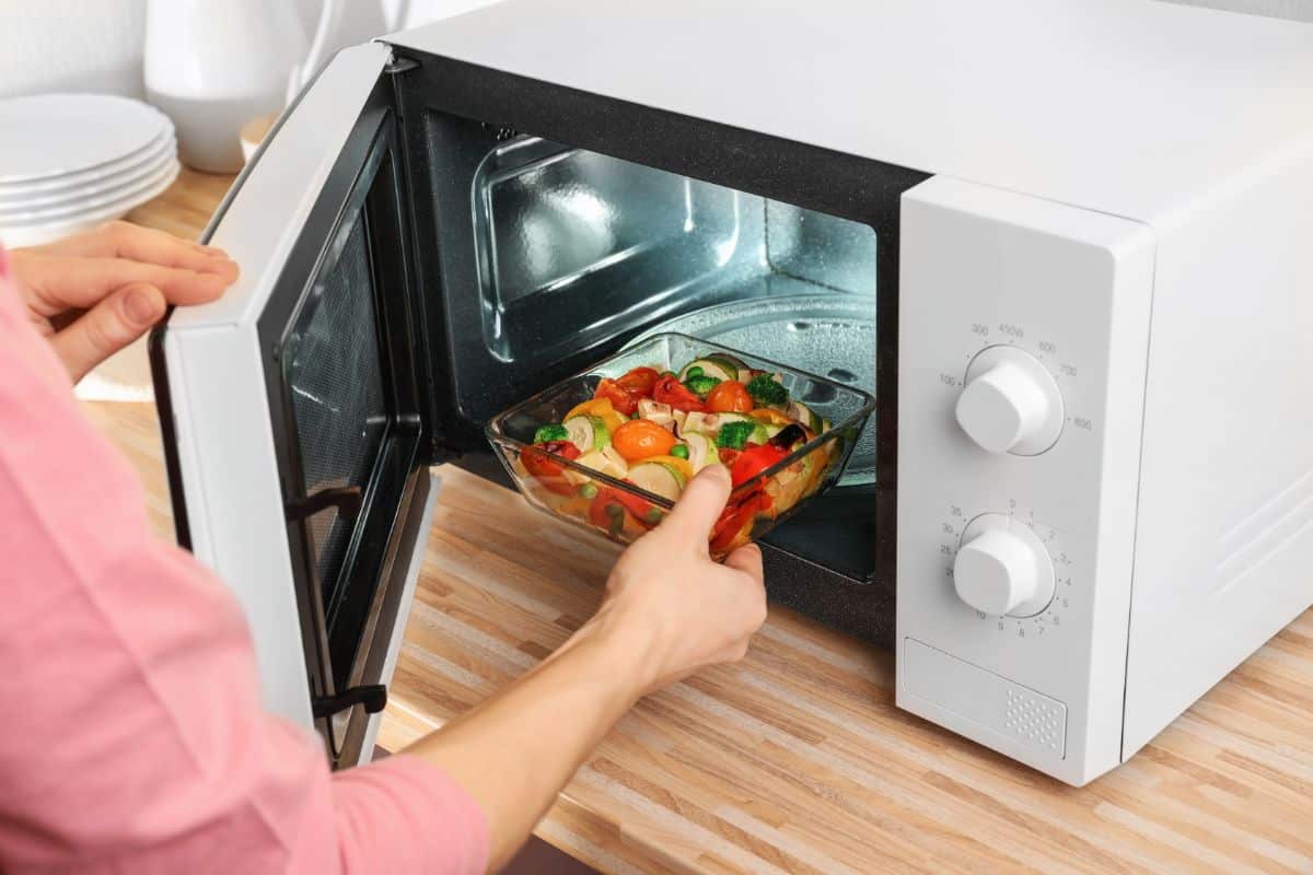 A man putting a meal in a glass container in a microwave.